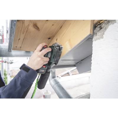 A person is sanding a wooden cladding with an electric sander. A scaffolding is visible in the background.