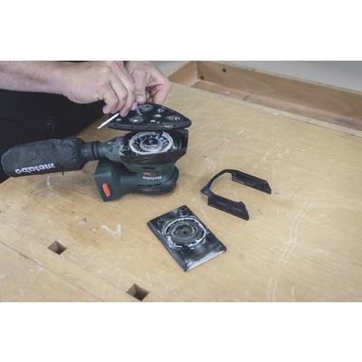A person is repairing an angle grinder on a wooden table, with the protective guard removed and spare parts lying nearby.
