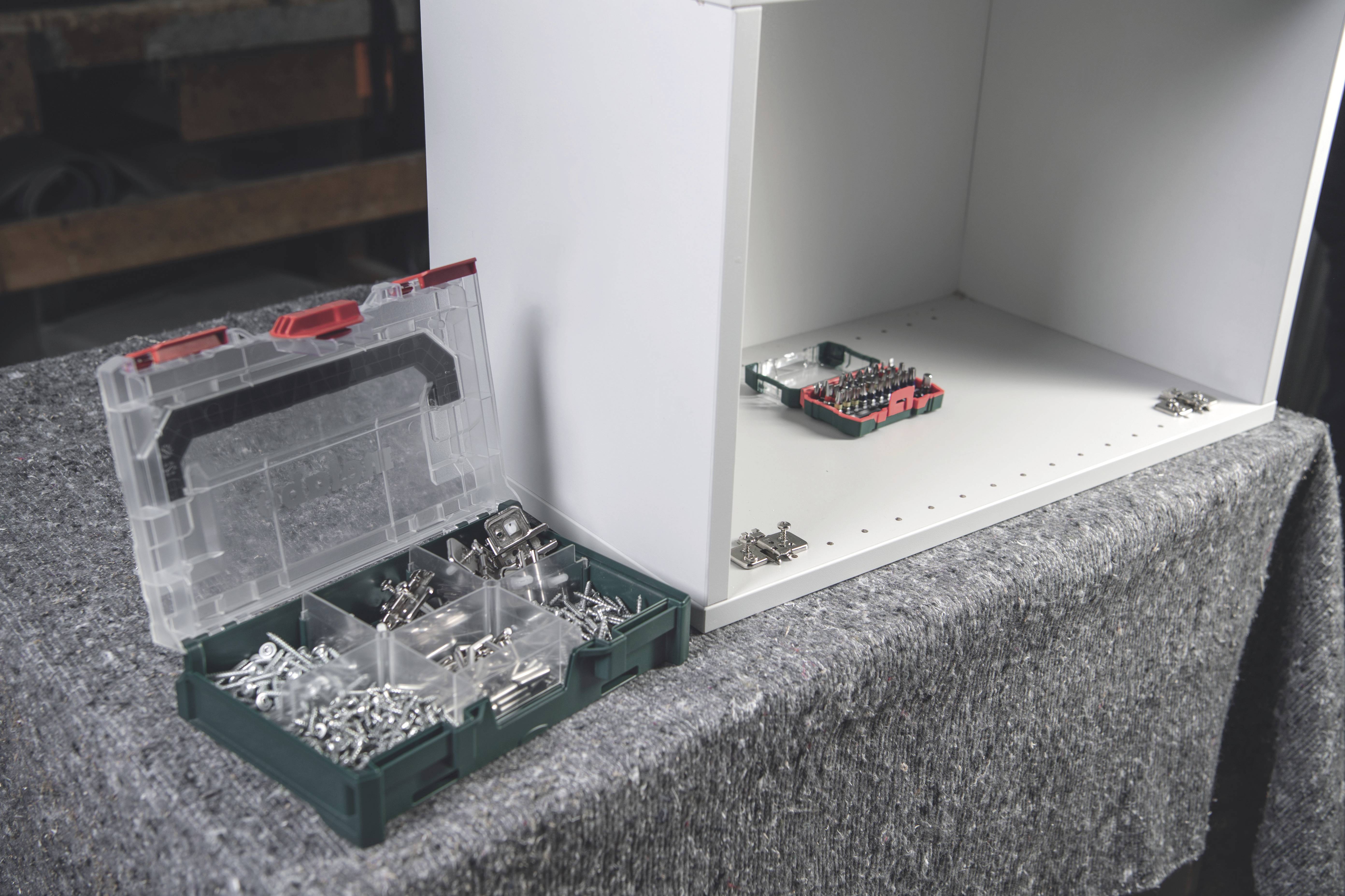 A toolbox with screws and nails stands open beside a half-assembled white cupboard on a table.