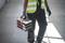 A person in workwear is carrying a toolbox in a light-filled environment.