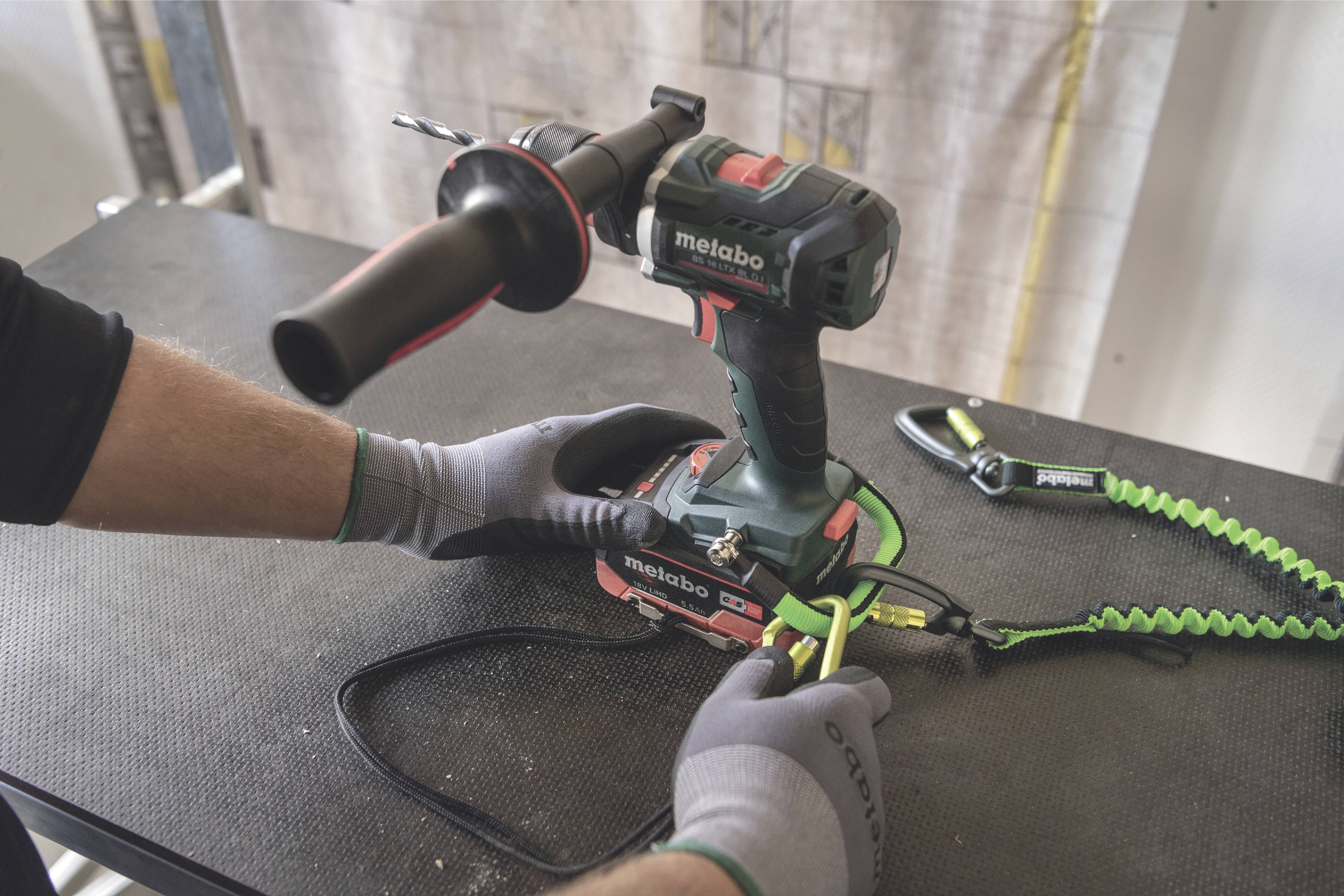 A construction worker wearing grey gloves secures a cordless drill on a mounting bracket to ensure safety during work.