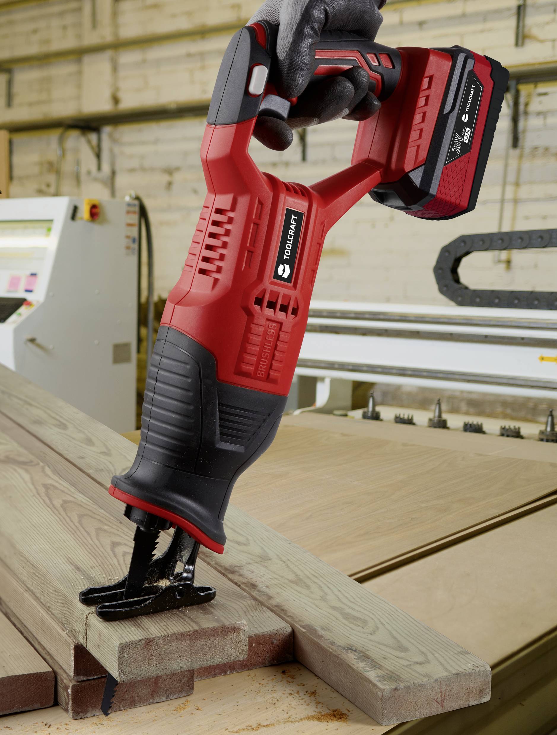 Reciprocating saw in use for cutting wood on a workbench in a workshop environment. Person holding the saw firmly.