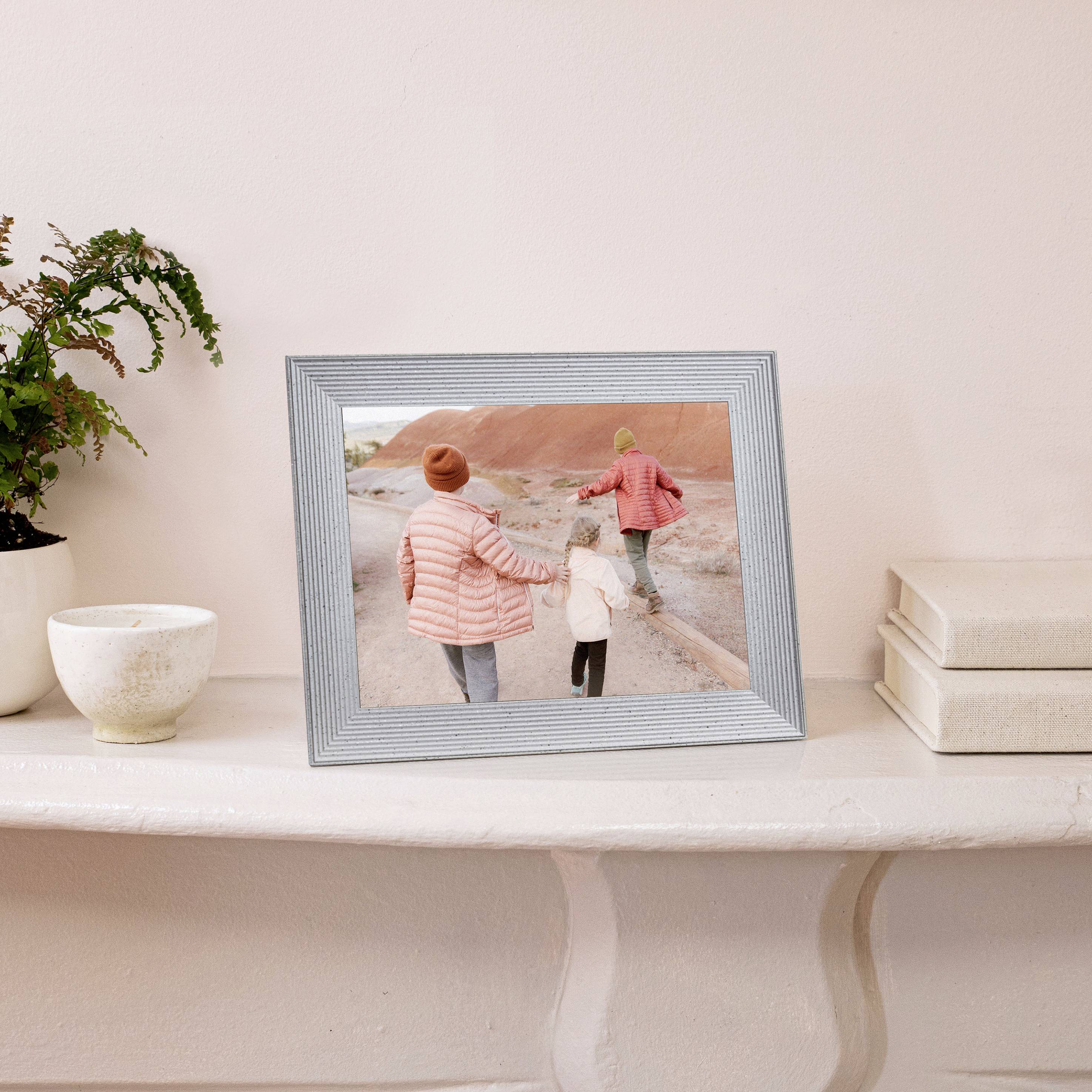 Framed photo on a mantelpiece: Two people in pink jackets walking through a tranquil landscape. Plants and books nearby.