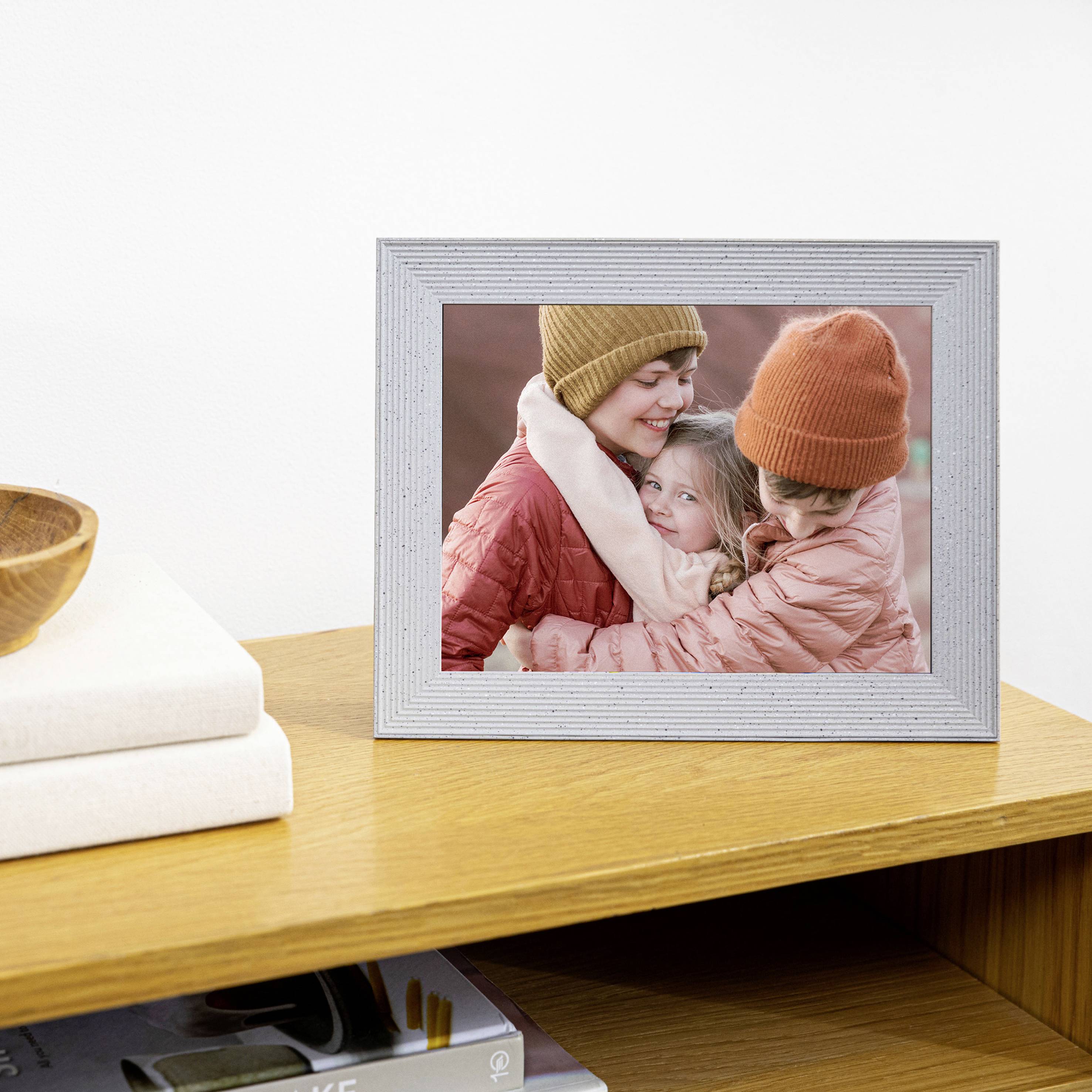 Framed photo of three people laughing and hugging, placed on a wooden table next to stacked books.