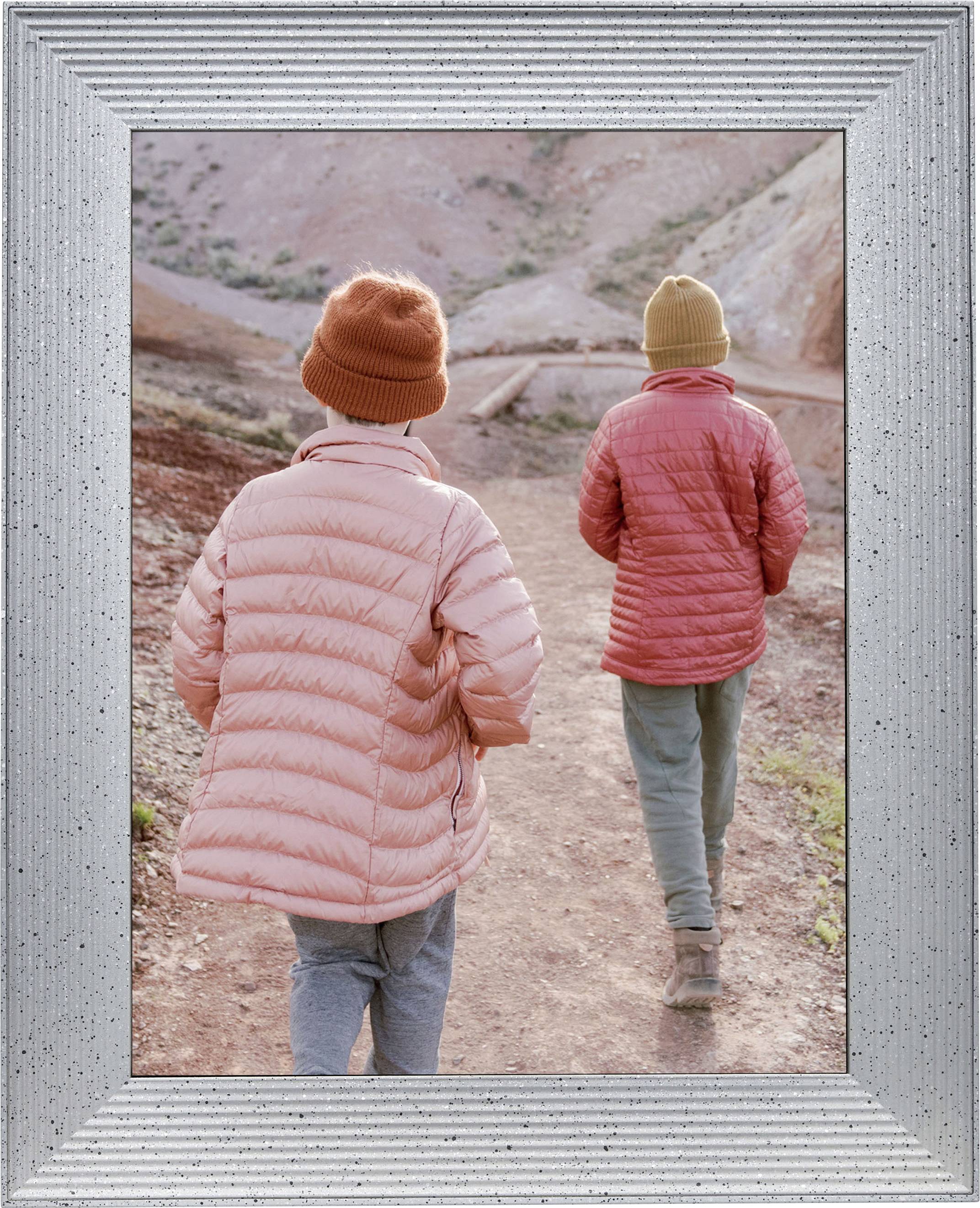 Two people in winter clothing are walking along a hiking trail. They are wearing orange hats and pink jackets on a sandy landscape.