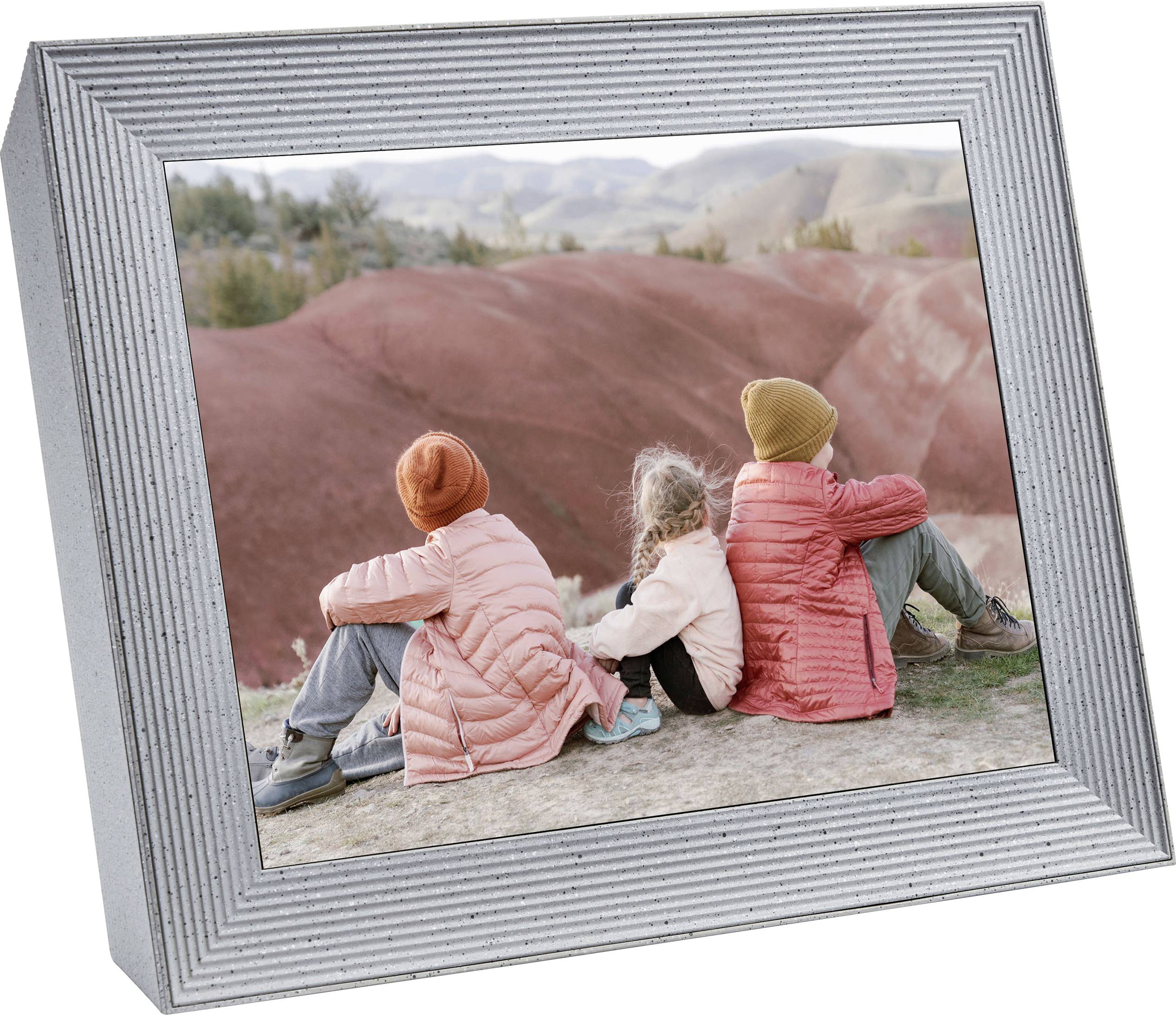 Three children in warm jackets are sitting on a hill, looking out over a landscape with red rocks in the distance.