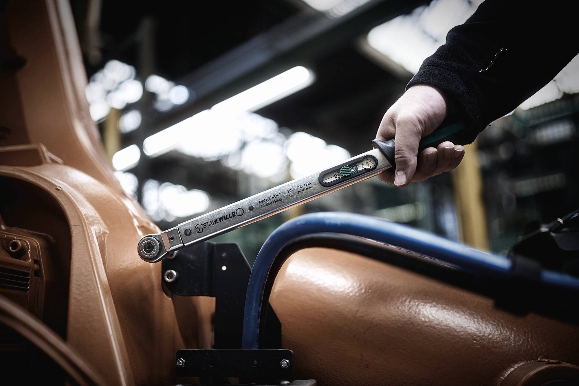 A person is using a torque wrench to tighten a screw on a machine in an industrial setting.