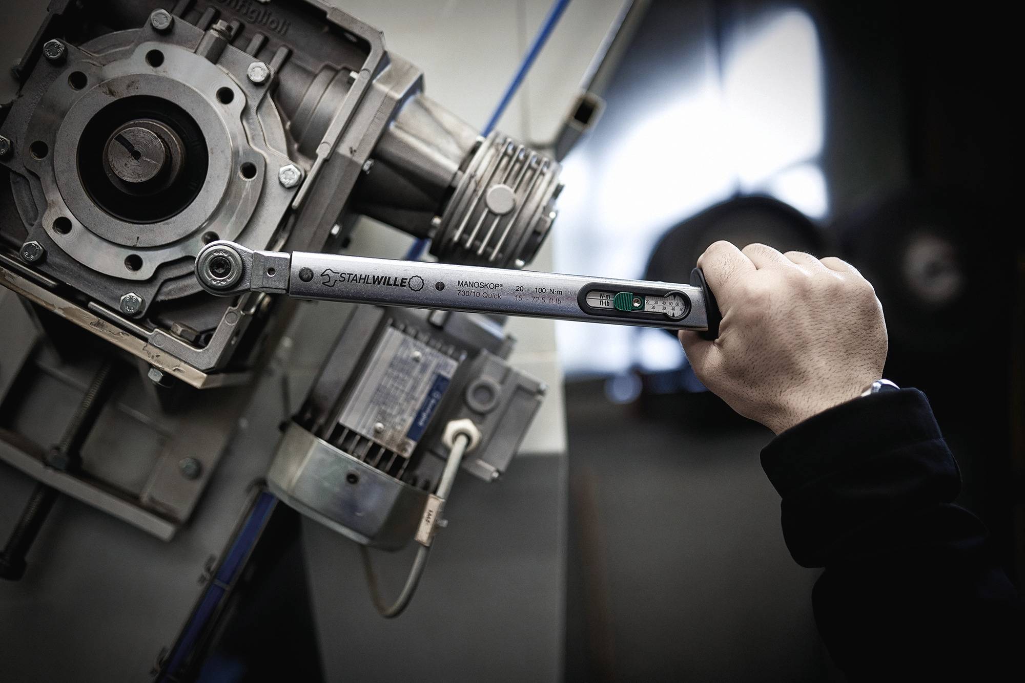 A person is using a torque wrench to tighten a screw on a machine component.
