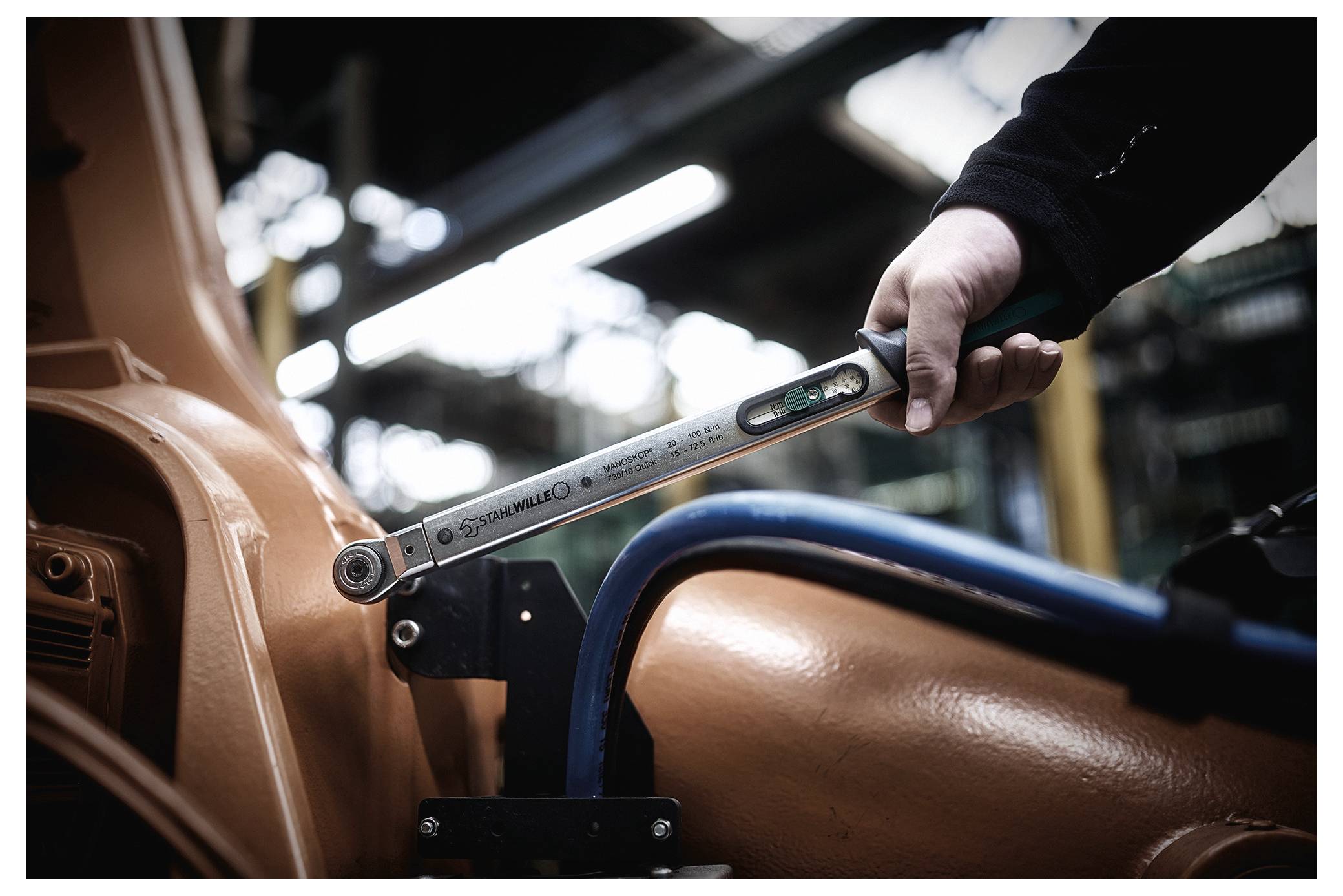 A person uses a torque wrench to tighten a bolt on machinery, indicating maintenance or assembly work in an industrial setting.