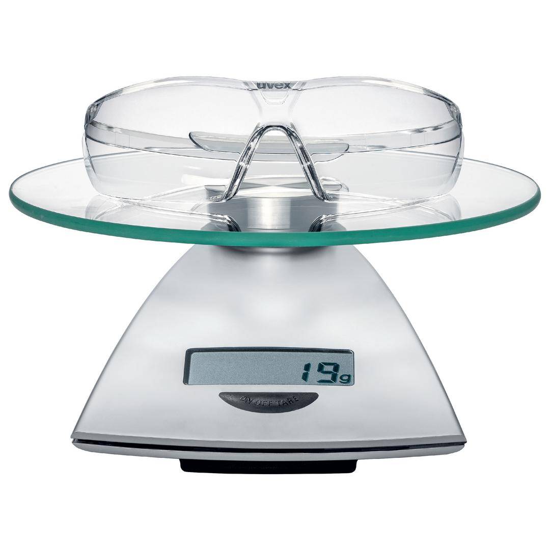 A pair of safety glasses rests on a digital scale, which displays 19 grams. The scale has a modern, silver design.
