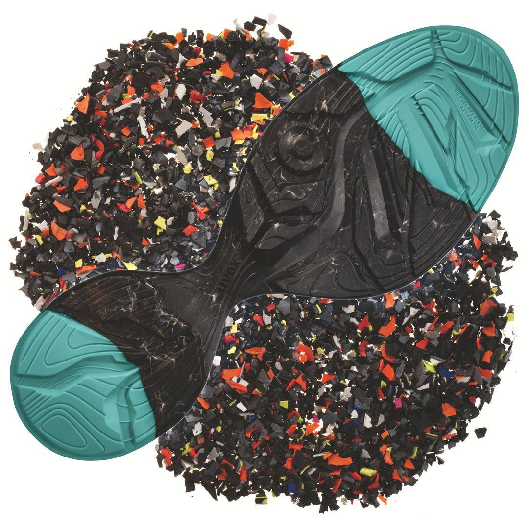A trainer lies upside down on a pile of colourful plastic pieces, with the sole and recycled material shown.