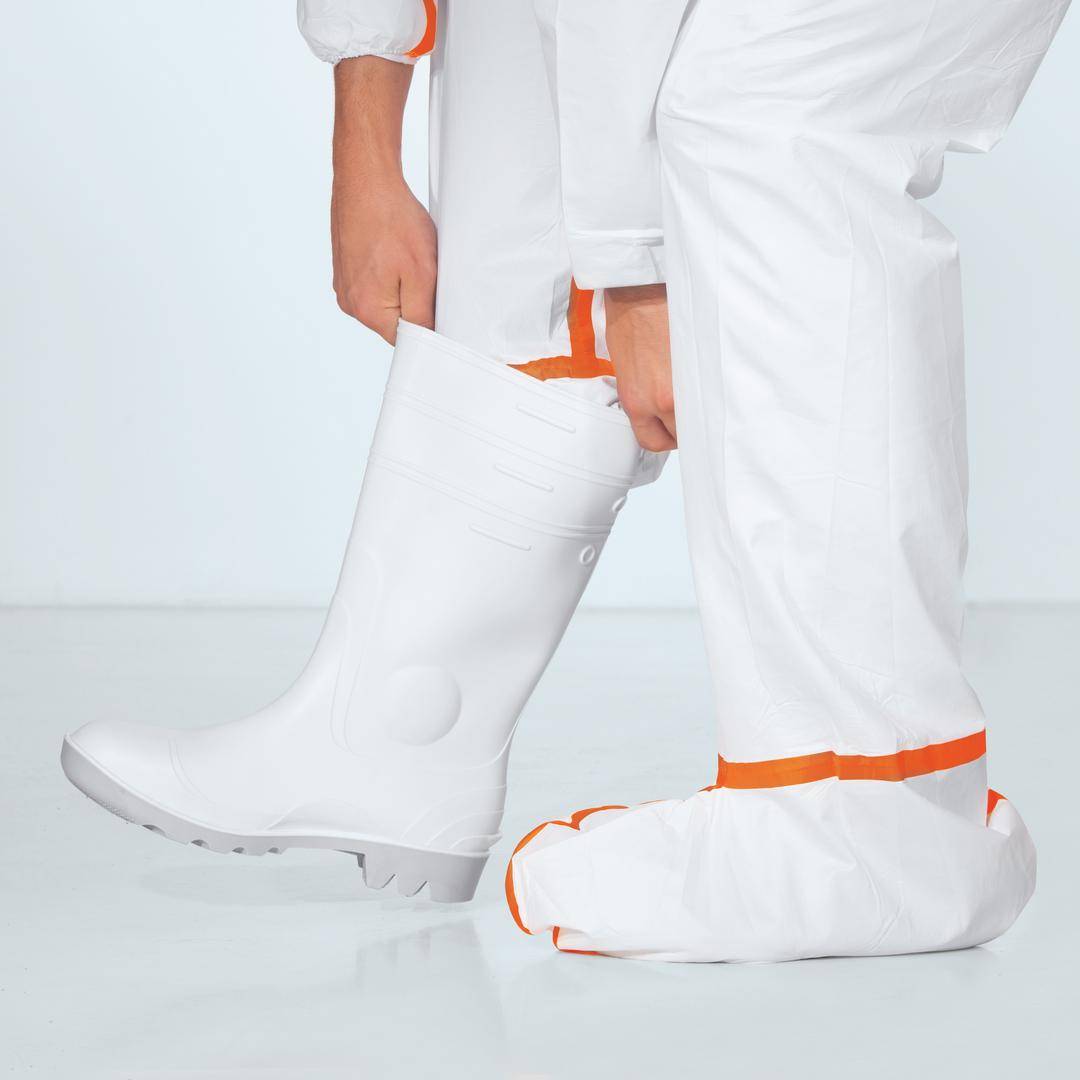 A person is wearing a white protective suit and white rubber boots.