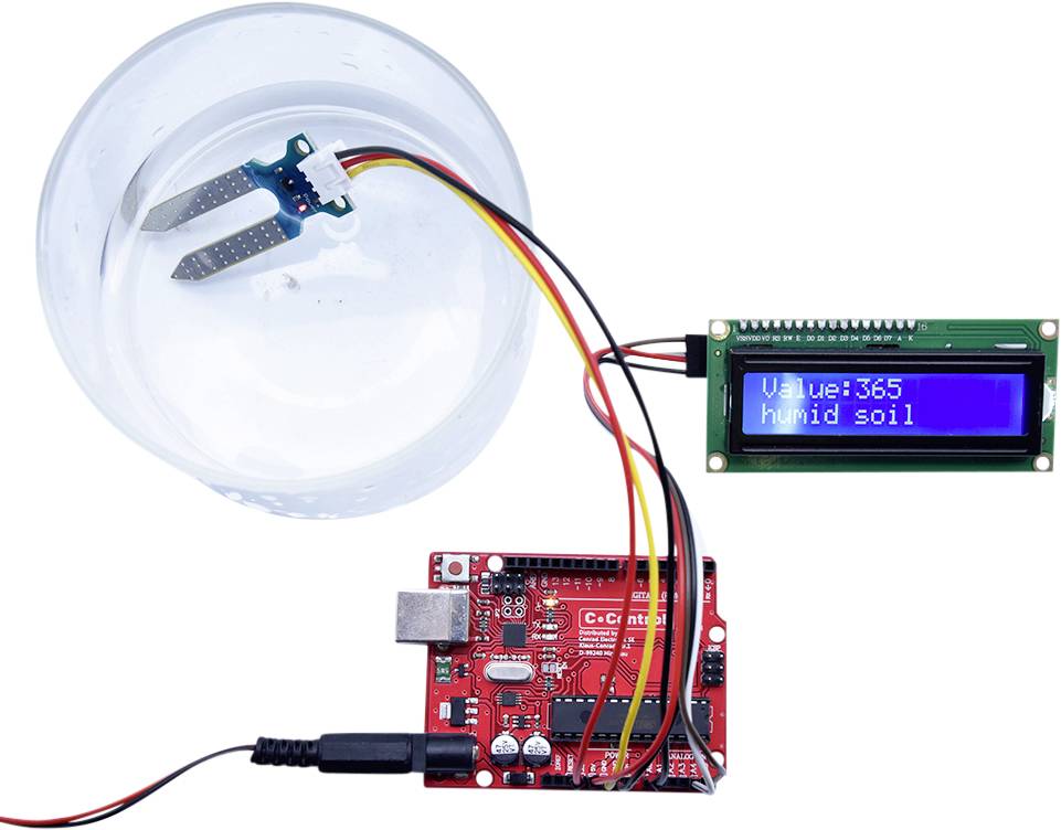 'Red Arduino microcontroller with moisture sensor connected in water. LCD displays: Value=365, damp soil.'