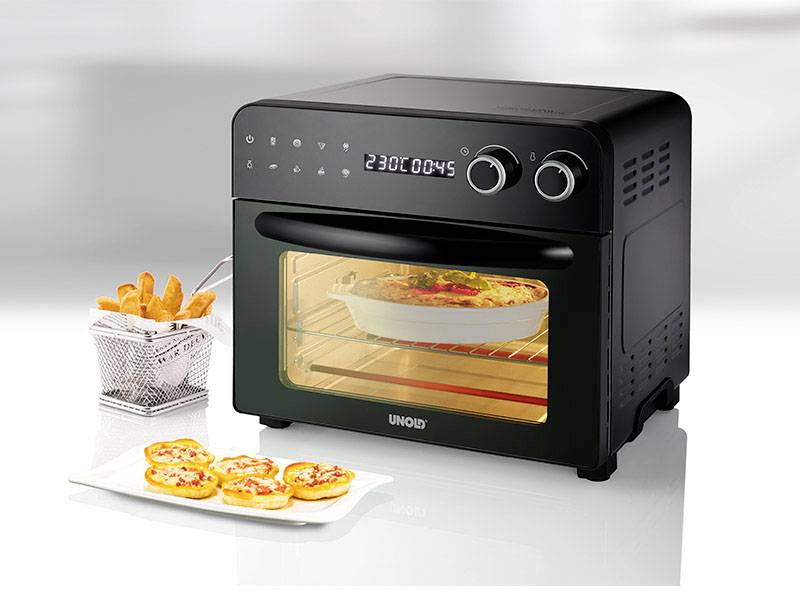 Black mini oven on white background, showing LED display '230C 00:45'. Filled baking dish inside, with a plate of mini pizzas and a deep-fat fryer basket beside it.
