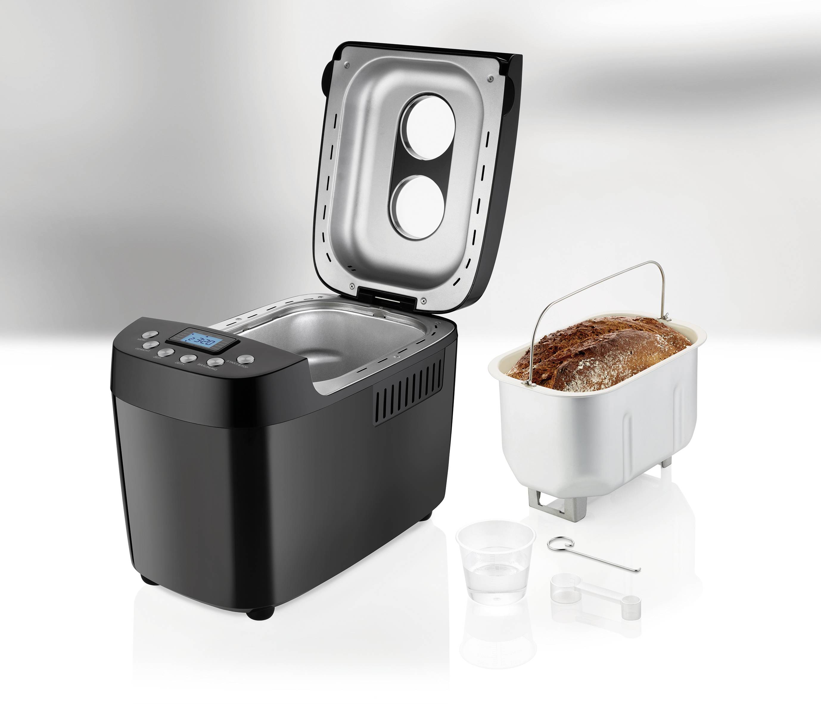 A black bread maker with its lid open, alongside a loaf of bread in a removable baking tin, a measuring jug, and a mixing hook.