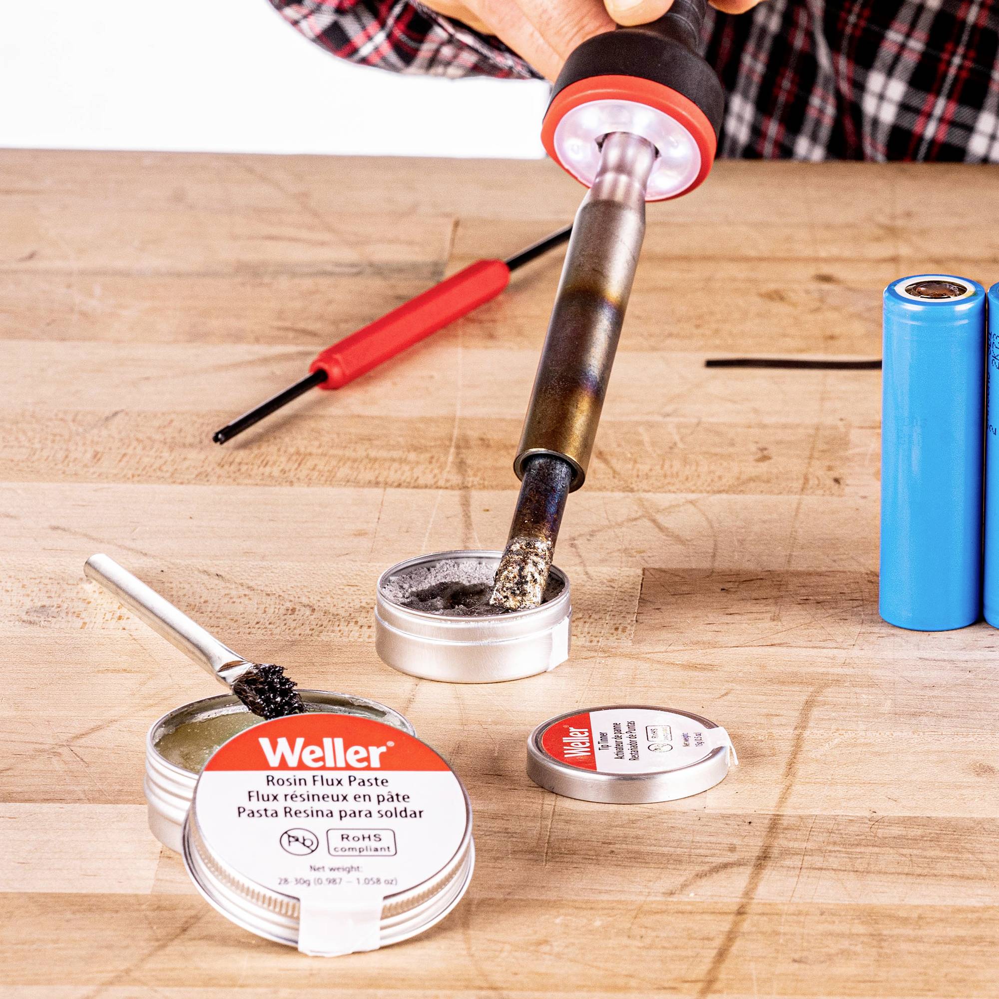 Soldering tool on wooden surface: A soldering iron with flux, two batteries and a screwdriver visible.