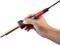 A hand is holding a soldering iron with a red handle. The soldering iron is ready for use, with cables leading upwards from the handle.