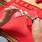A person is soldering an electrical circuit on a red work surface. Hands are holding a soldering iron and a wire.