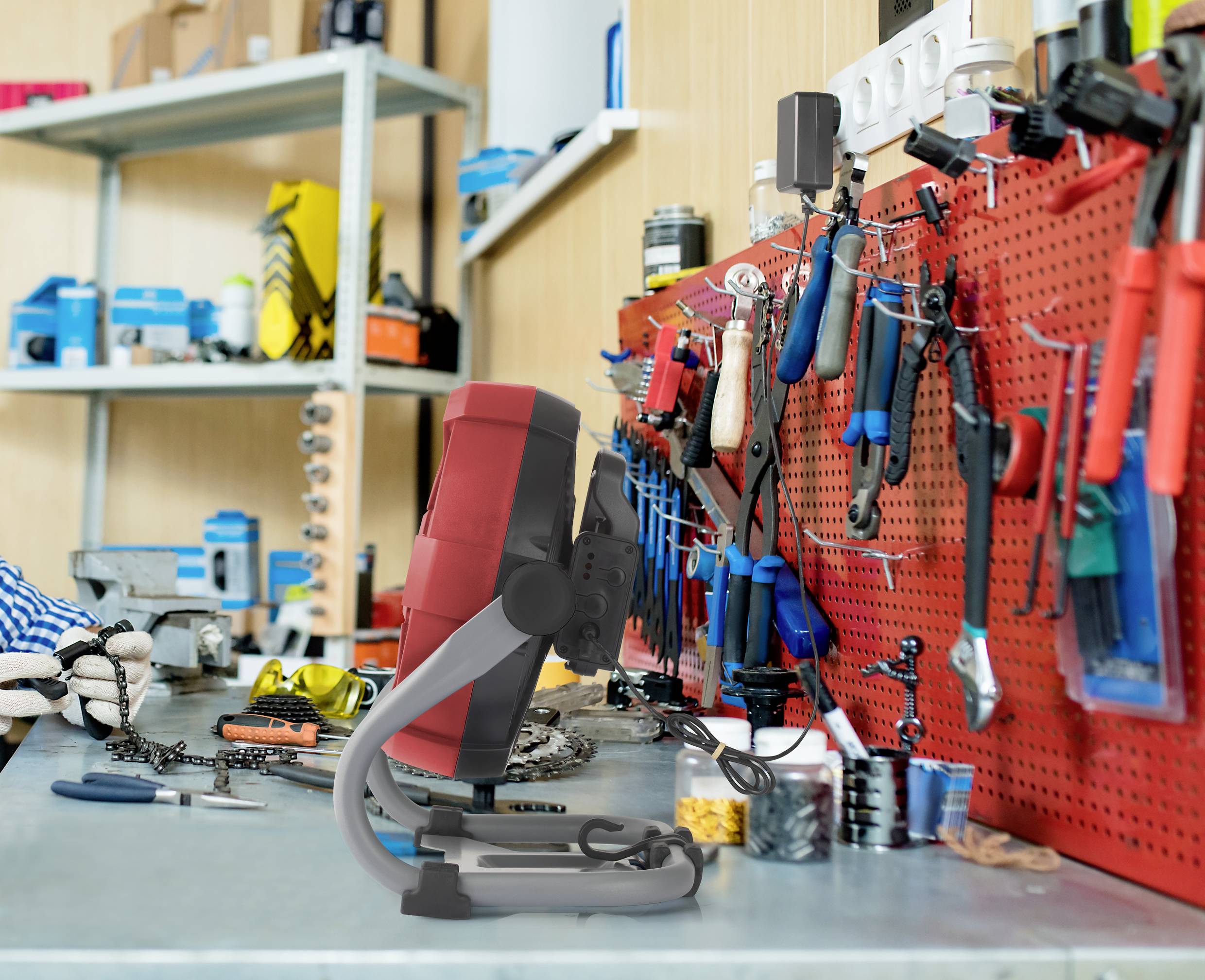 A brightly lit workshop bench with a 3D printer in the foreground. Various tools are neatly arranged hanging on the wall.
