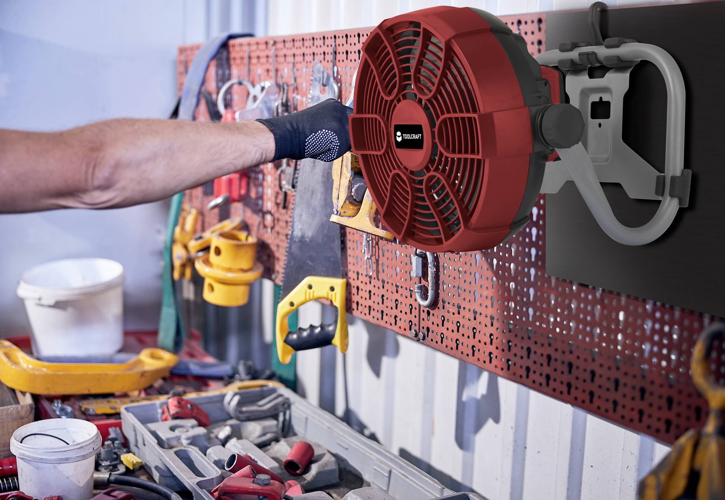 A person is hanging a red extension pipe on a wall mounting in a workshop. Tools are visible in the foreground.