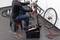 A person is repairing a bicycle mounted on a stand. Tools and a toolbox are scattered around them on the ground.