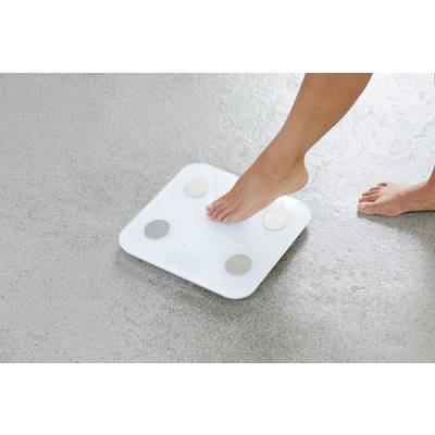 A foot approaches a white personal weighing scale on a grey floor. The scale has four metal sensors for weight and body measurement.