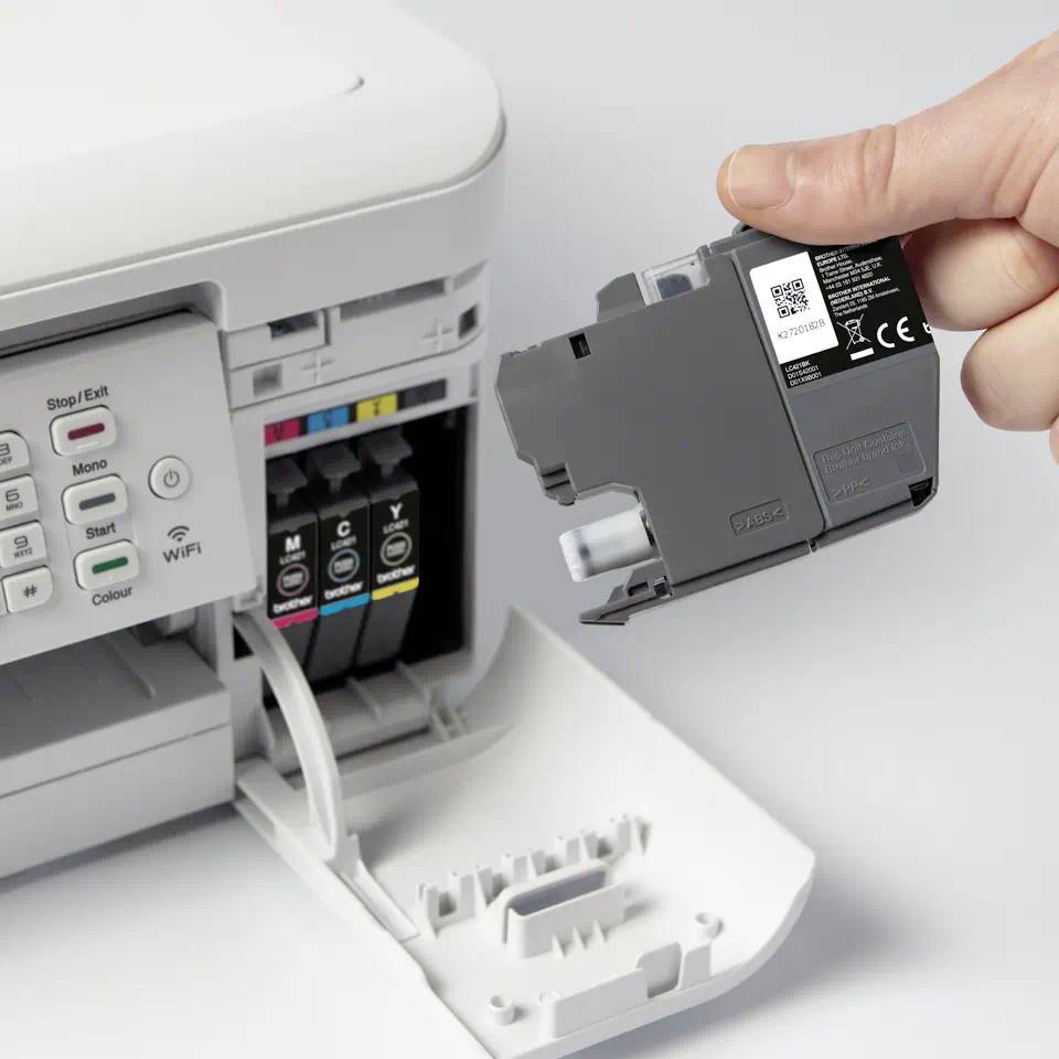 A hand is replacing an ink cartridge in a colour printer. The printer cover is open, and the colour cartridges are visible.