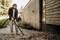 A man is using a leaf blower to clear autumn leaves from a gravel path beside a modern wooden house.