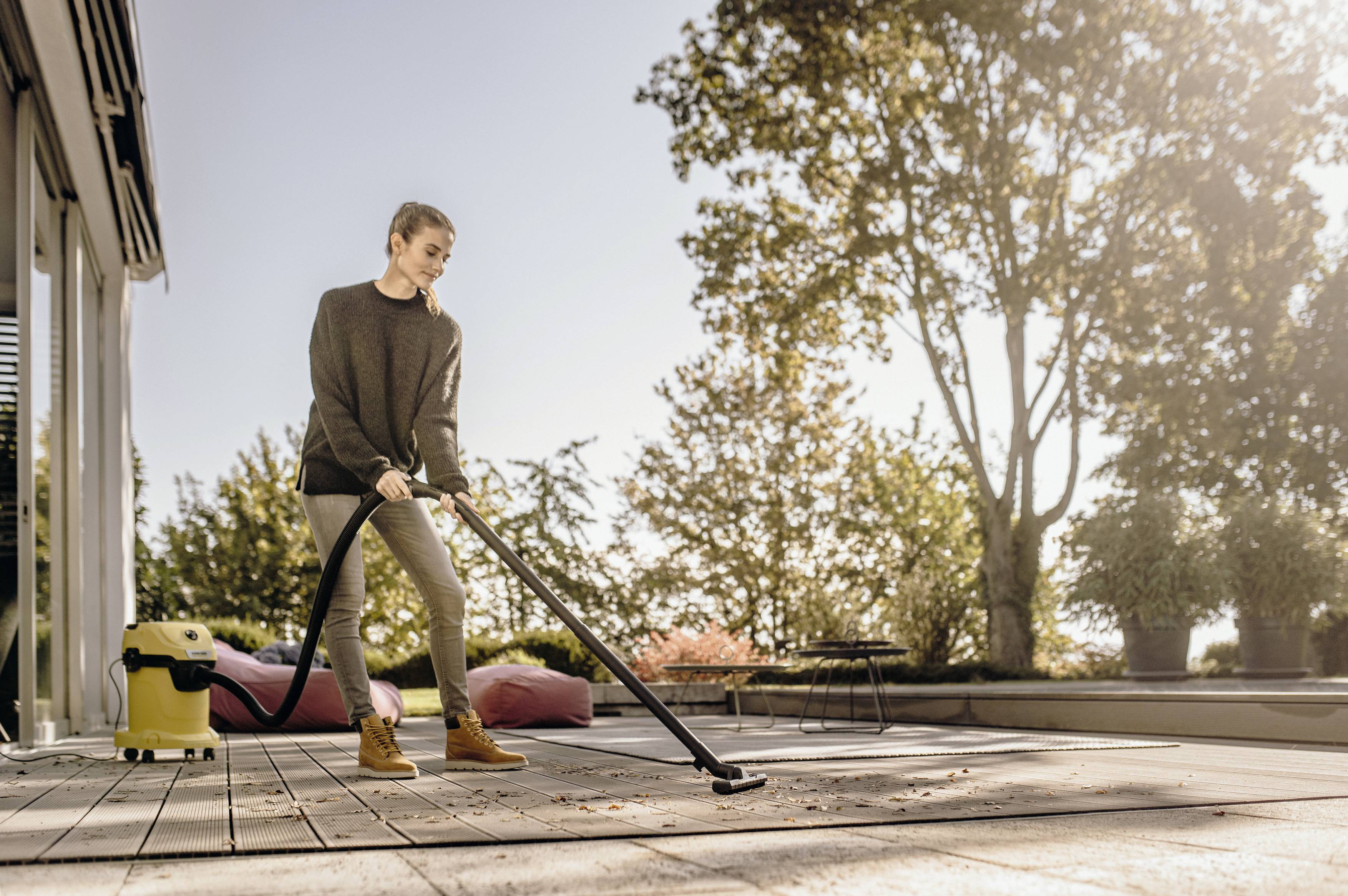 A person is cleaning a patio with an industrial vacuum cleaner on a sunny day. Trees are visible in the background.