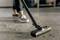 A person is hoovering a dirty floor. Only the shoes and the vacuum cleaner are visible while dirt is being removed.
