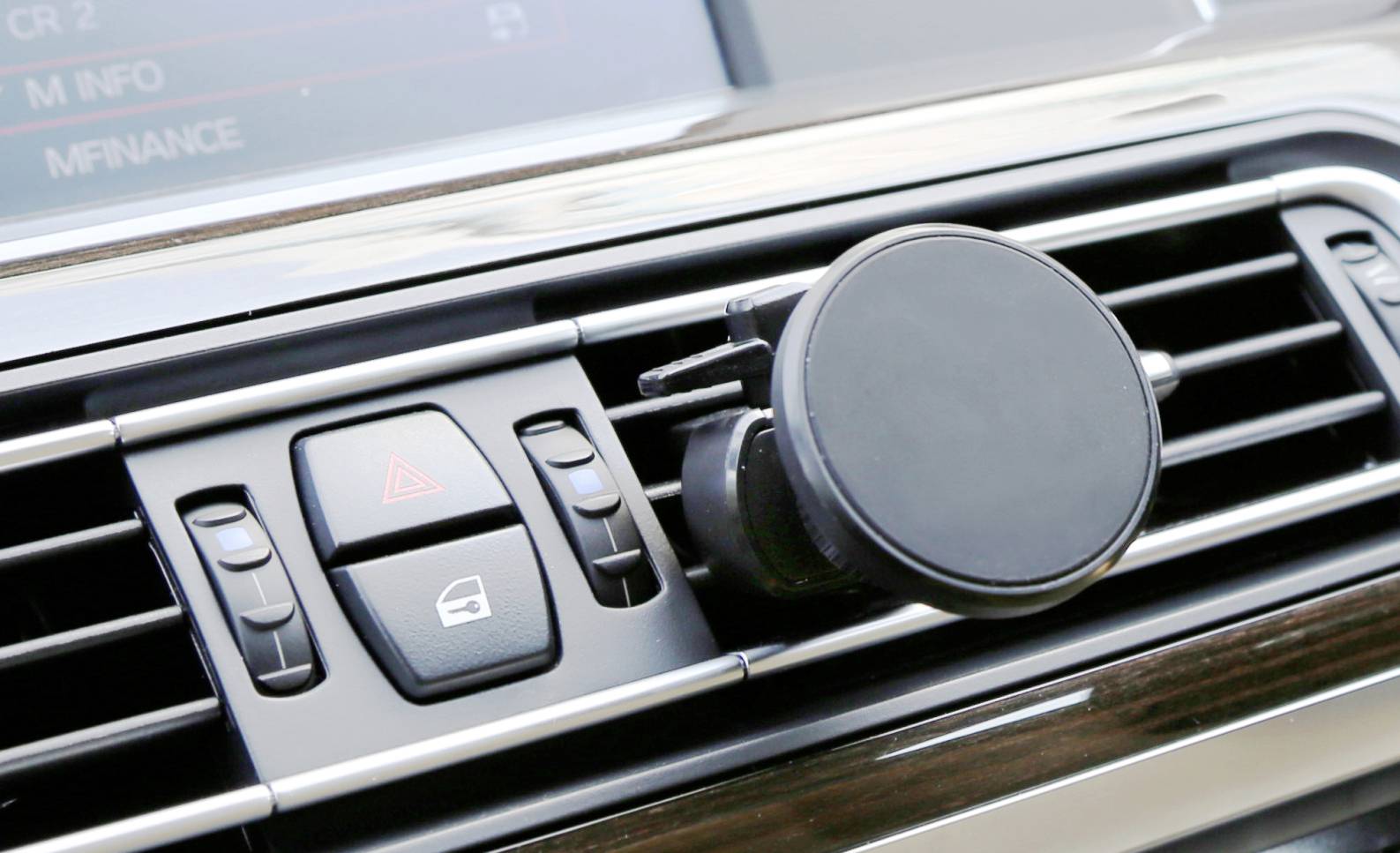 A smartphone mount is attached to the air vents of a car. Beside it are buttons for vehicle controls.