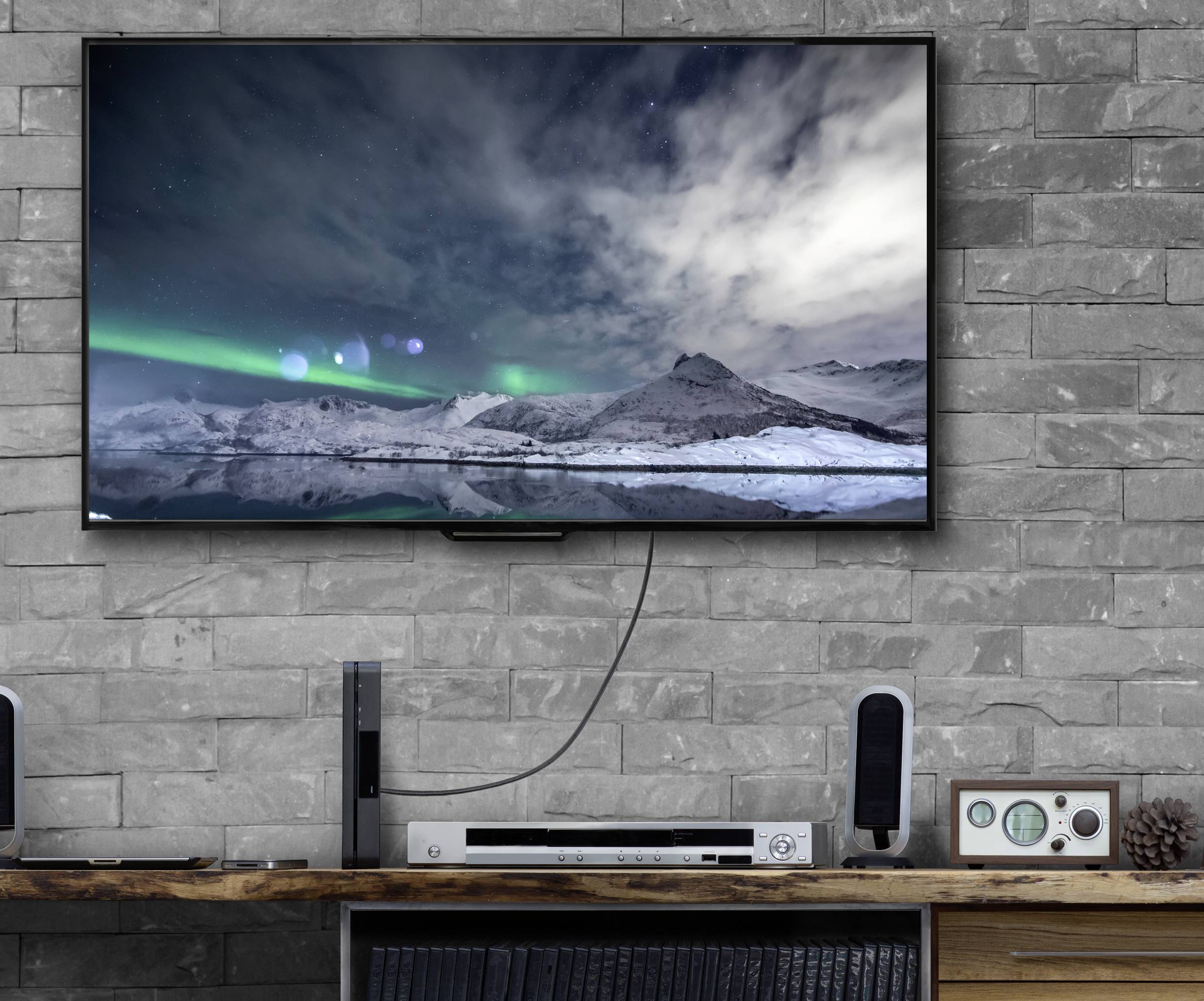 A television mounted on a grey brick wall displays an image of snow-covered mountains beneath a night sky illuminated by a greenish aurora.