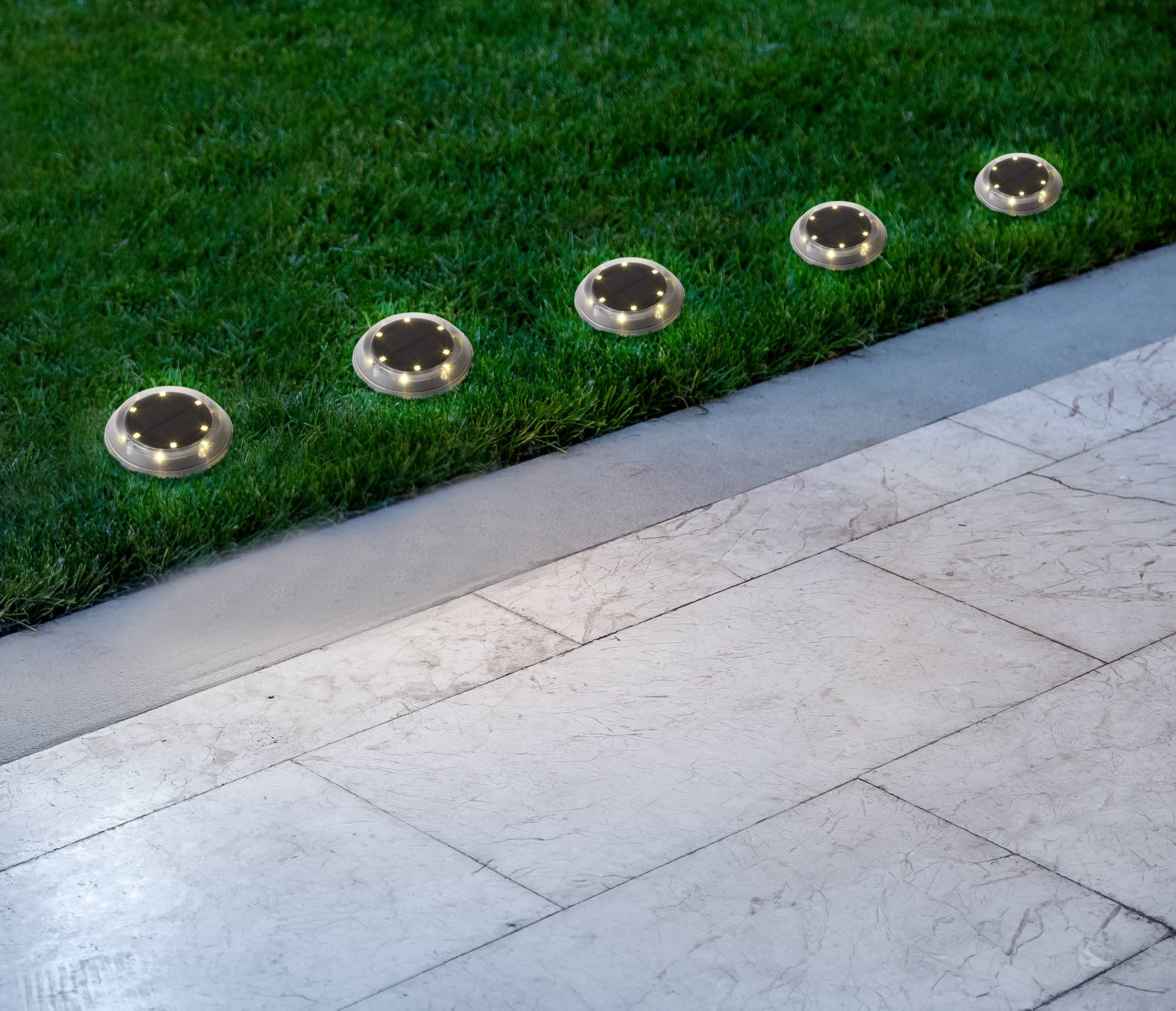 Solar-powered ground lights on a lawn beside a footpath. Lights glow softly and are evenly spaced.