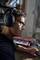 A person is wearing headphones and working at a mixing desk in a sun-filled room, with a plant in the background.