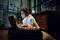 A person wearing headphones is working intently on a laptop in a cosy-looking room with subdued lighting.