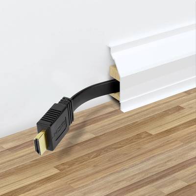 A black HDMI cable emerges from beneath a white skirting board and lies on a wooden floor.