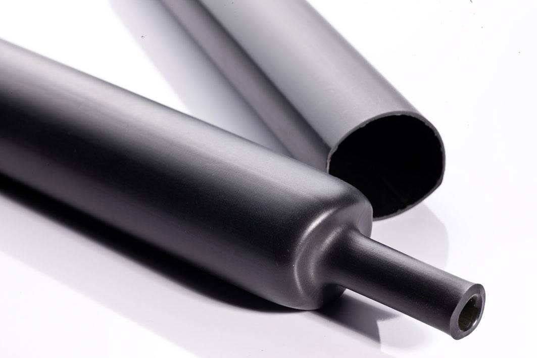 Two black pipes are lying side by side. One of the pipes is open at the end, the other has a flat closure.