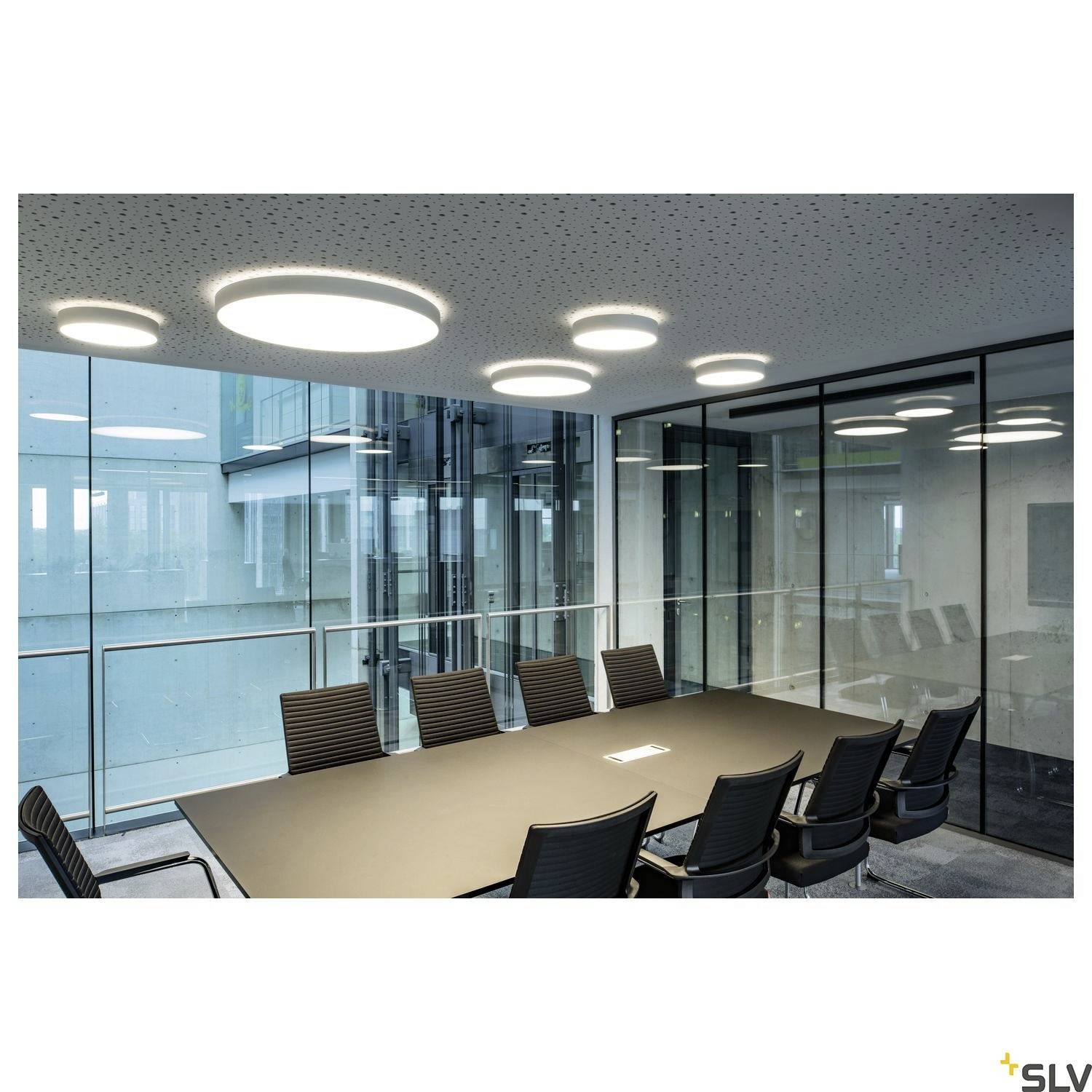 Conference room with a large rectangular table and ten black chairs, surrounded by glass walls. Modern ceiling lights are visible.
