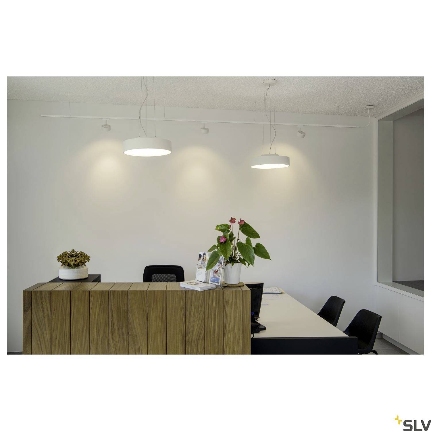 Reception area with a wooden counter, flowers in a vase, brochures, computer screens and four chairs in a modern, illuminated space.
