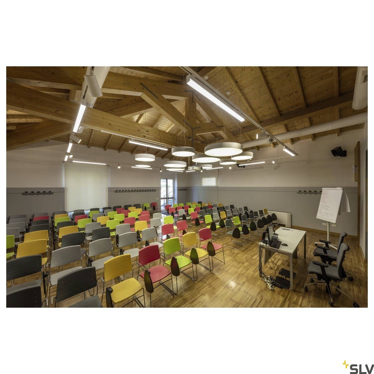 A modern, well-lit conference room with a wooden ceiling is before you. The room is equipped with colourful chairs and a presentation lectern.