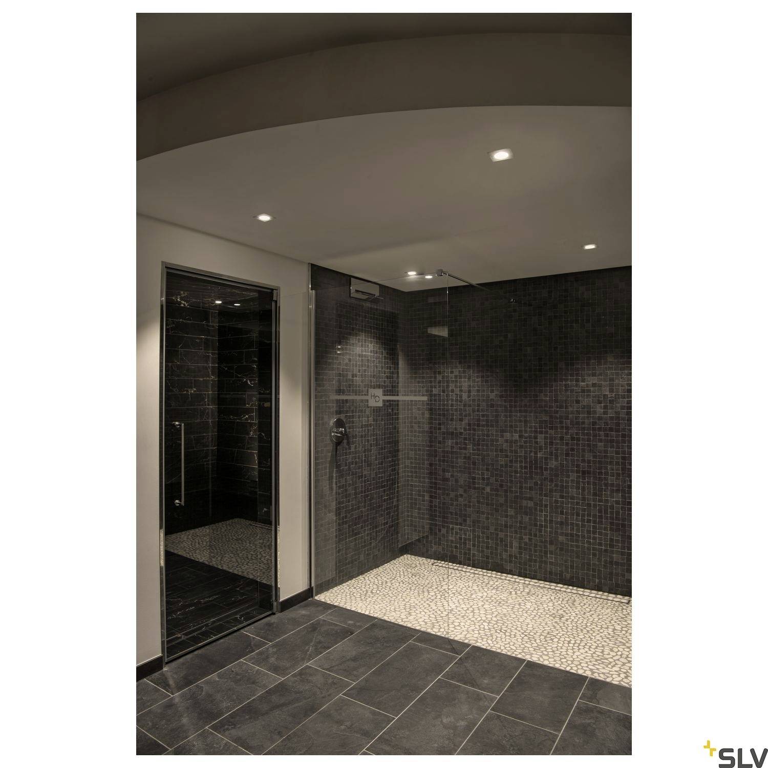 Modern shower with dark walls, glass partition and recessed ceiling lights. Floor with pebble pattern and dark tiles.