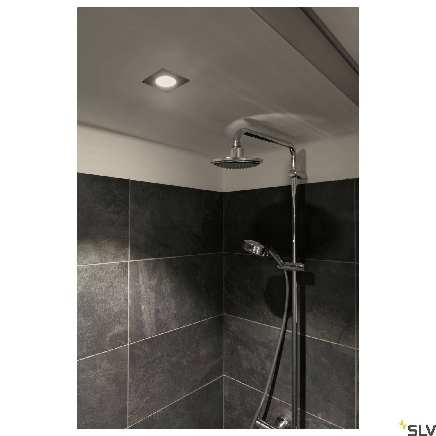 A illuminated shower enclosure with dark tiles and a modern rain shower head, mounted against the wall.