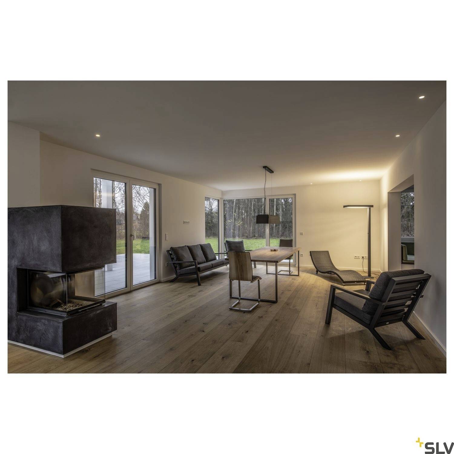 Living room with a fireplace, wooden flooring and large windows overlooking a garden. Modern furniture in muted colours.