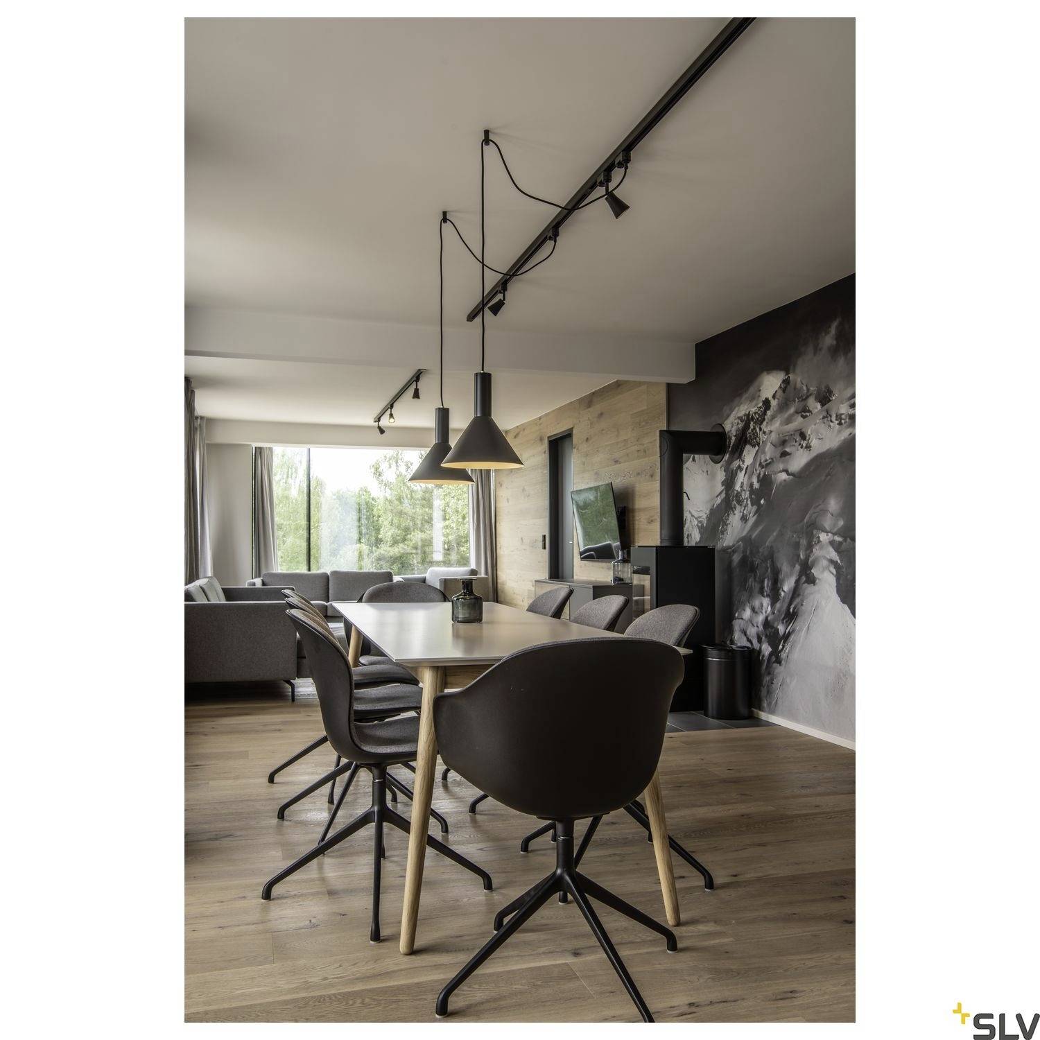 Modern dining area with wooden flooring and a large table, surrounded by black chairs. In the background, a cosy living room is visible.