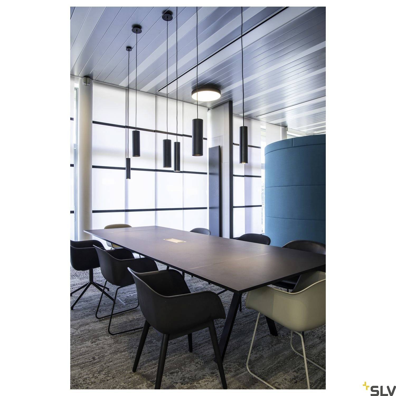 Modern meeting room with a long table, surrounded by black chairs. Large windows allow plenty of light to enter.