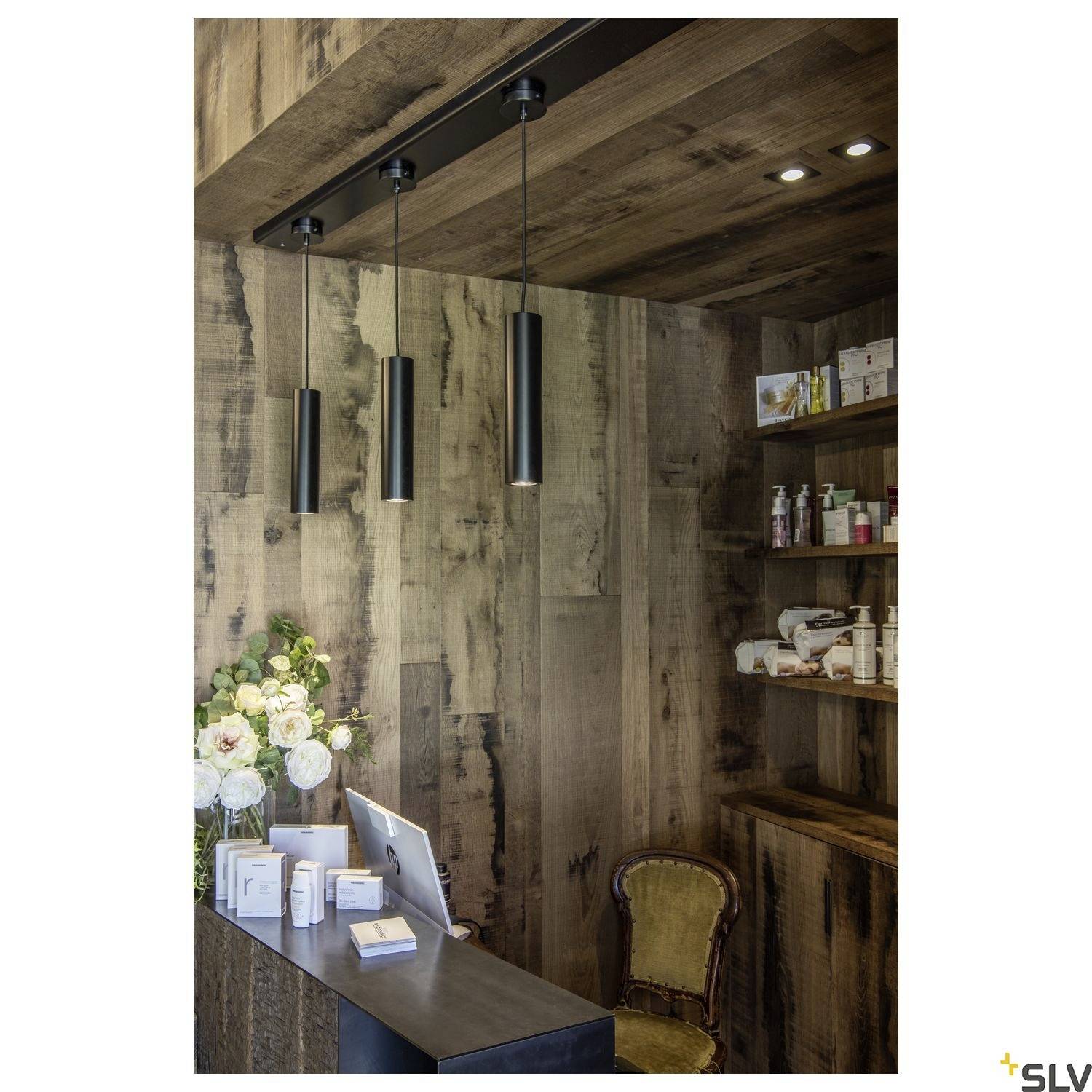 A wooden, stylish reception area with hanging lamps, a laptop, flowers, and shelves stocked with care products.