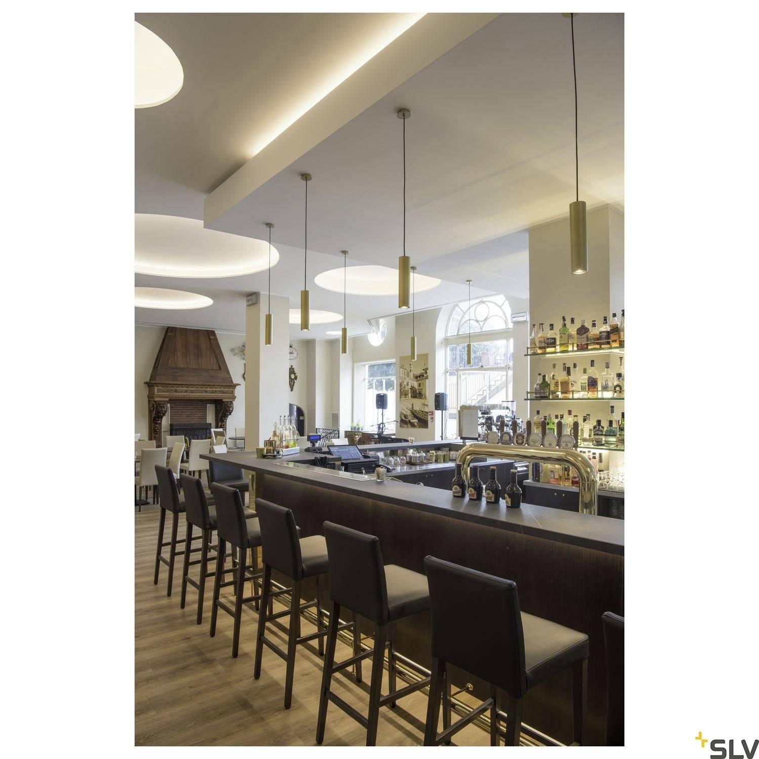 A modern café with a long counter, bar stools, illuminated shelves full of bottles, and stylish hanging lamps.