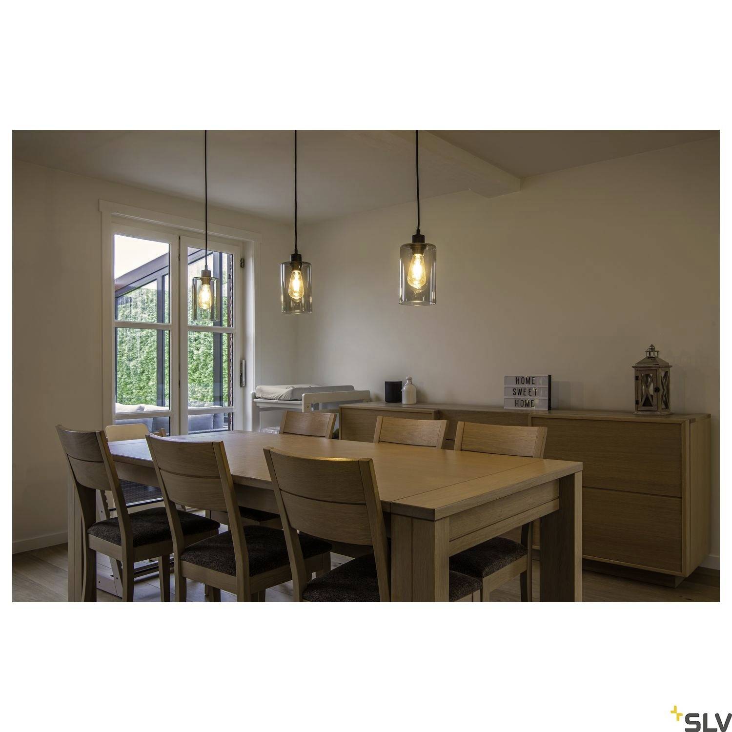 Dining room with a wooden dining table and six chairs. Three pendant lights illuminate the space. A window is located on the left in the background, offering a view outside.