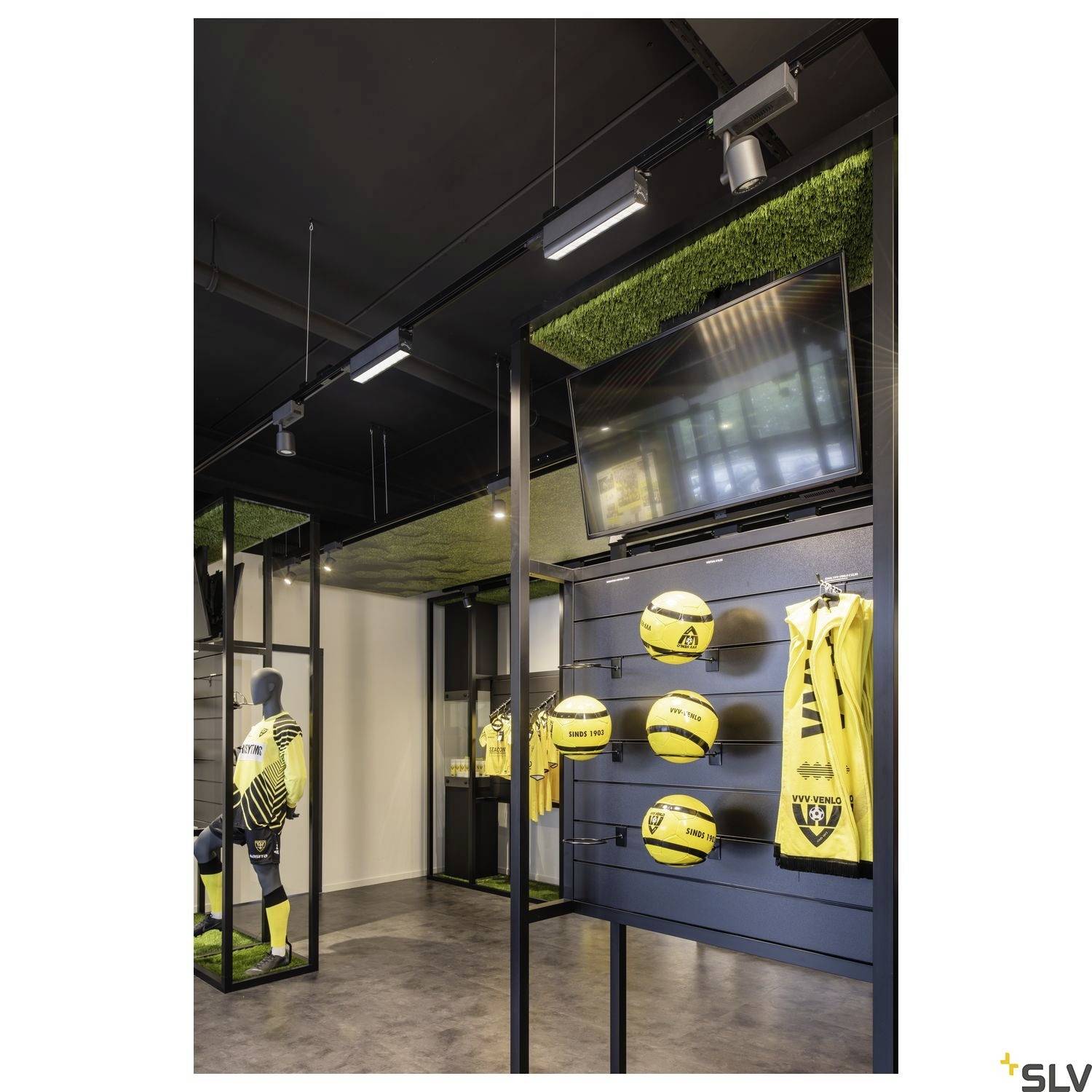 The interior of a sports shop displays yellow and black football jerseys, footballs on shelves, and a television wall mounted on the ceiling.