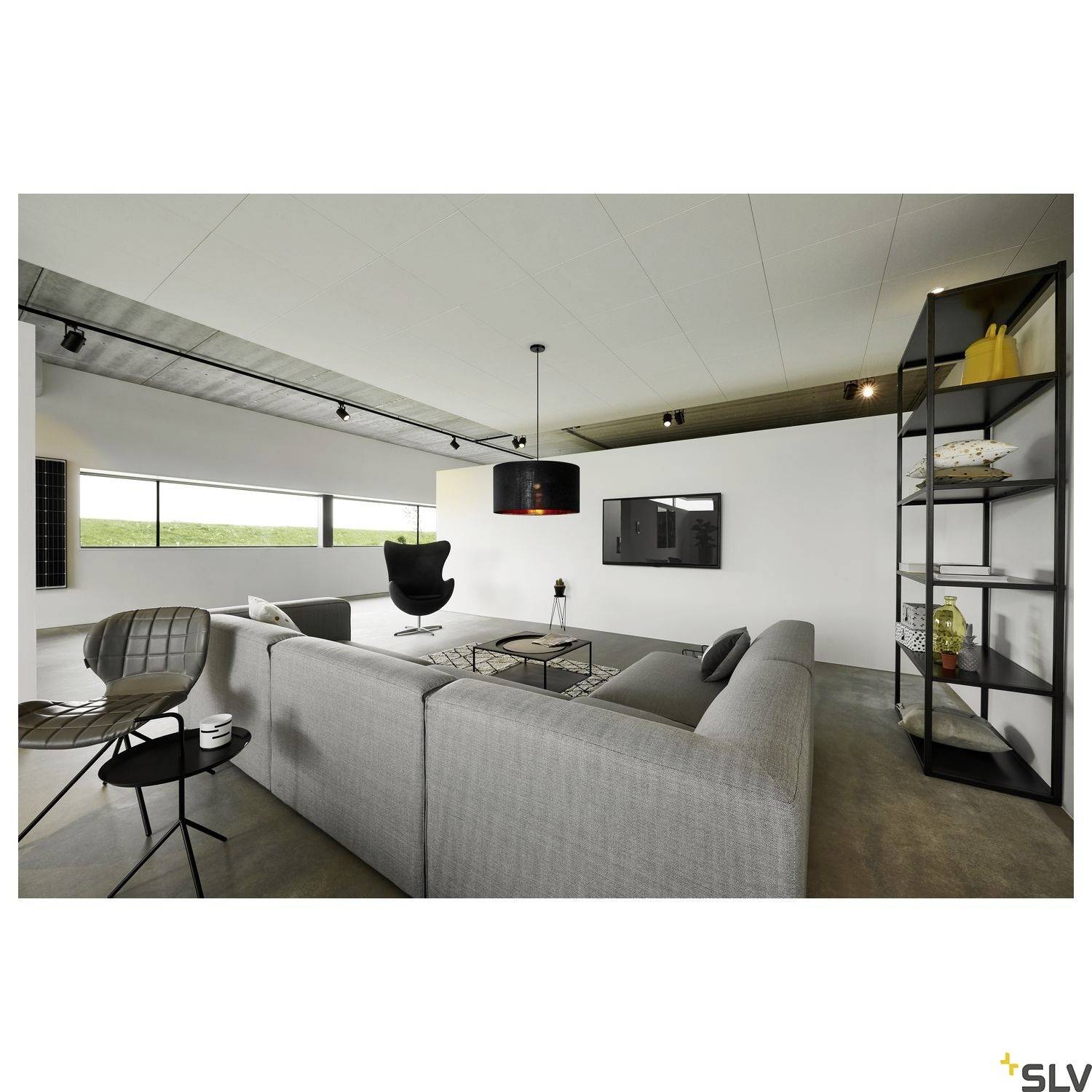 Modern living room with grey sofa, black chair, small table, pendant light, shelving unit, and view of landscape through window.